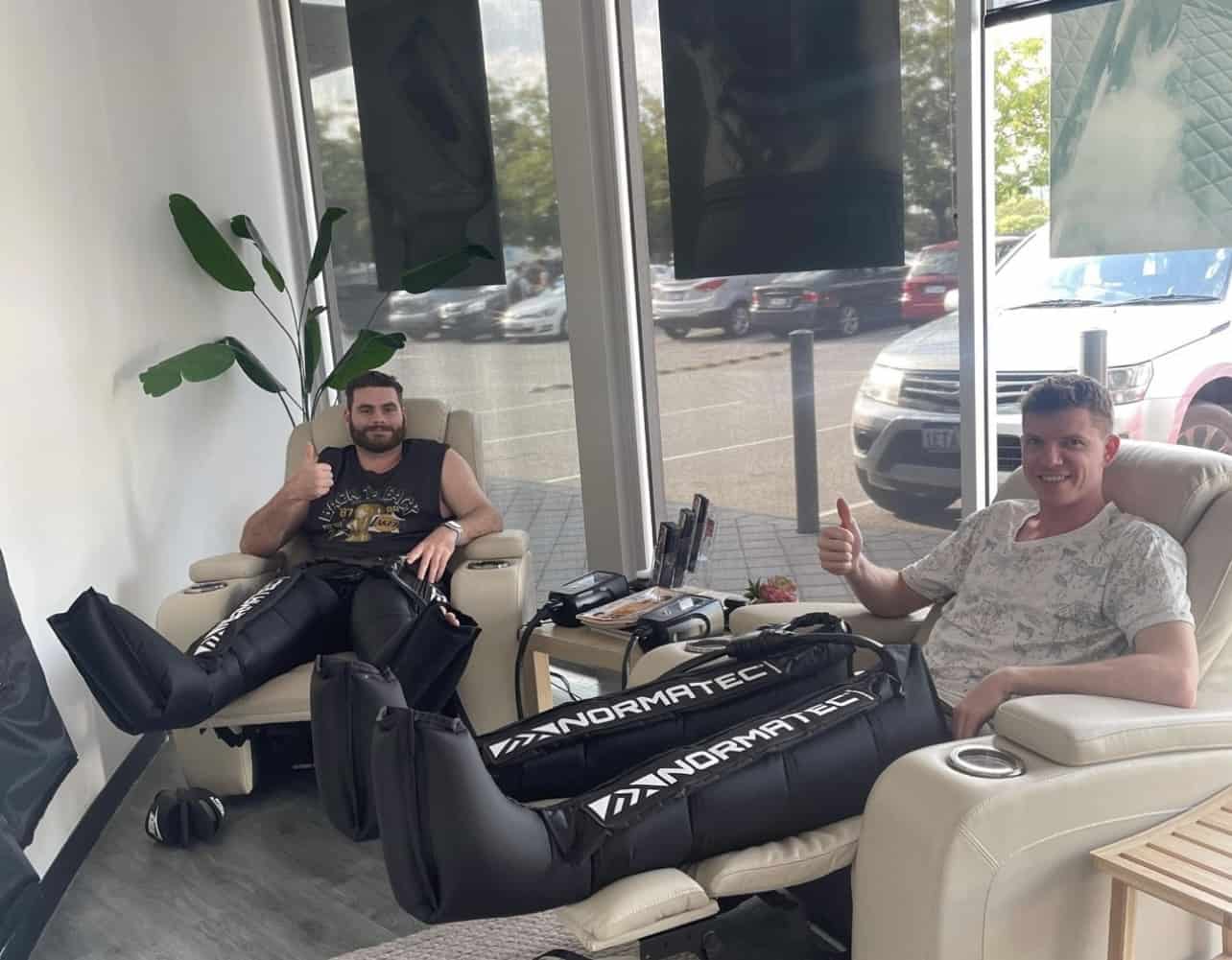 Two young men relaxing while using NormaTec compression boots
